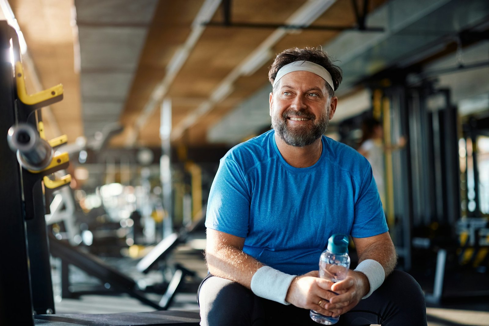 Happy mature sportsman during water break in health club looking away,
